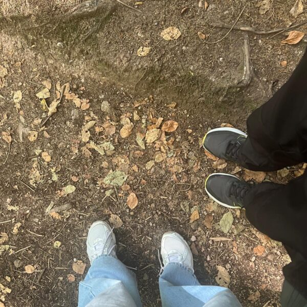 Blick nach unten auf zwei Paar Sneaker auf einem Waldboden mit Herbstlaub und Wurzeln.